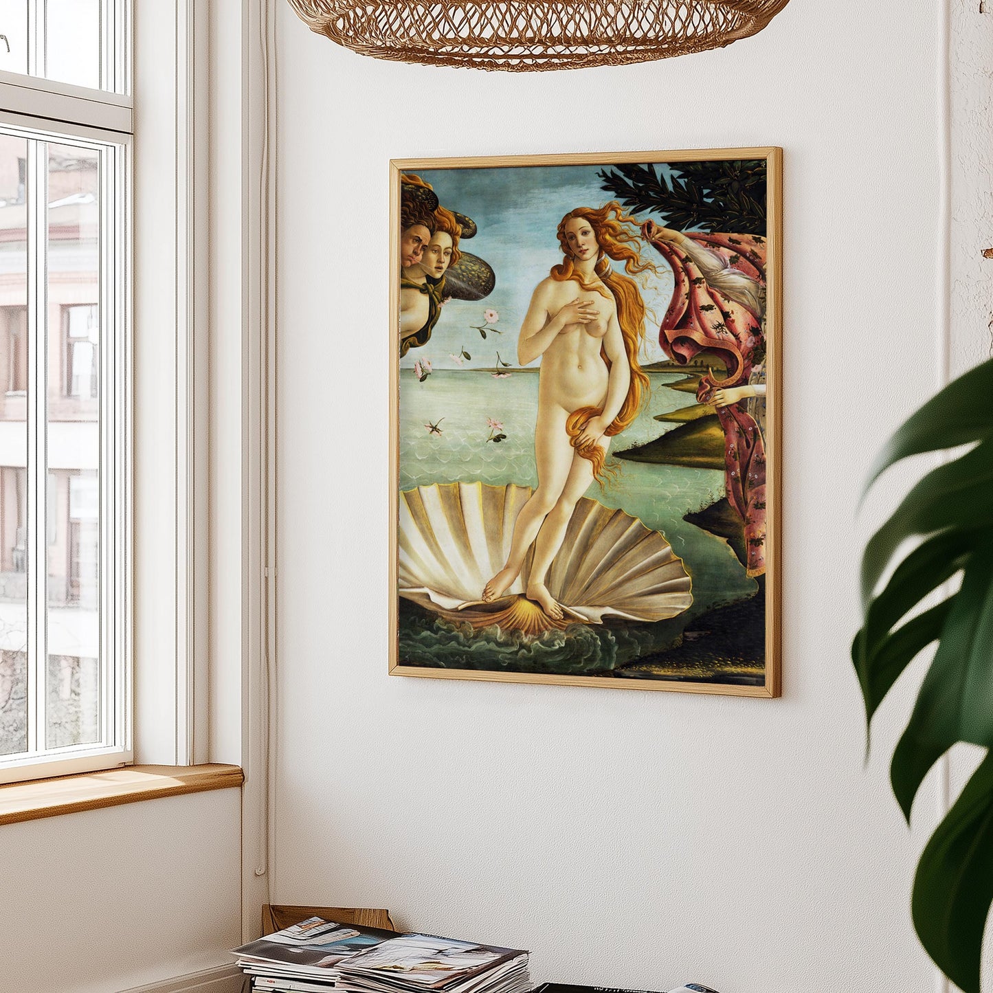 Botticelli's geboorte van venus poster aan witte muur, met links een raam en rieten lampenkap erboven – plant rechts in beeld.