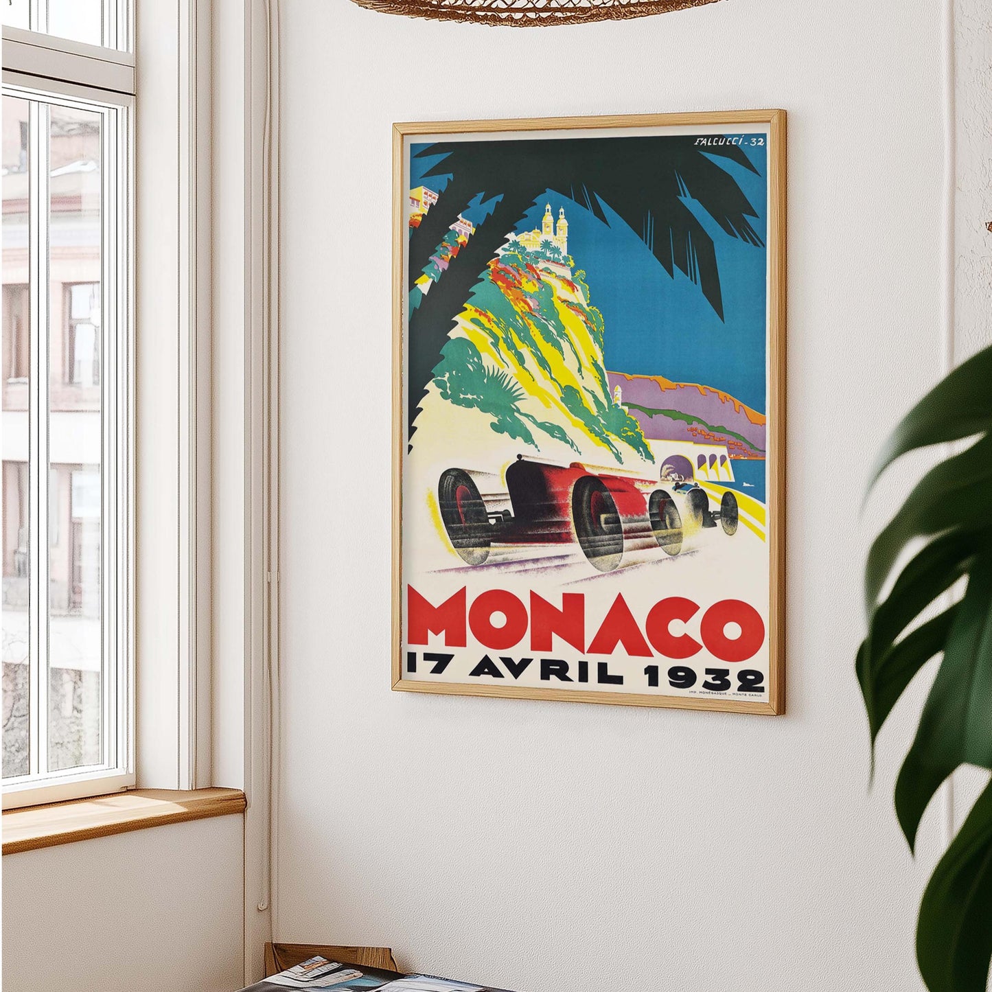Race poster aan witte muur, met links een raam en rieten lampenkap erboven – plant rechts in beeld.