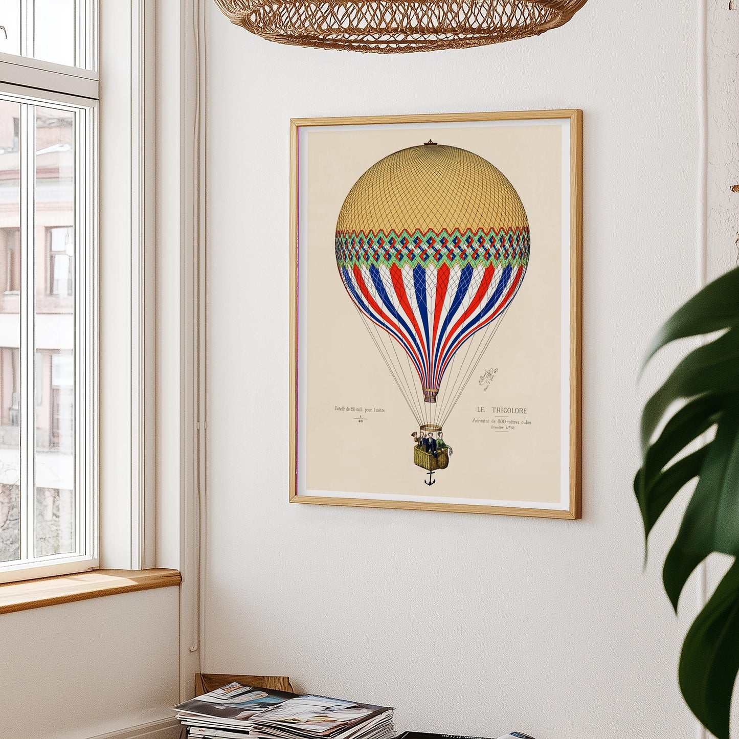 Luchtballonposter aan witte muur, met links een raam en rieten lampenkap erboven – plant rechts in beeld