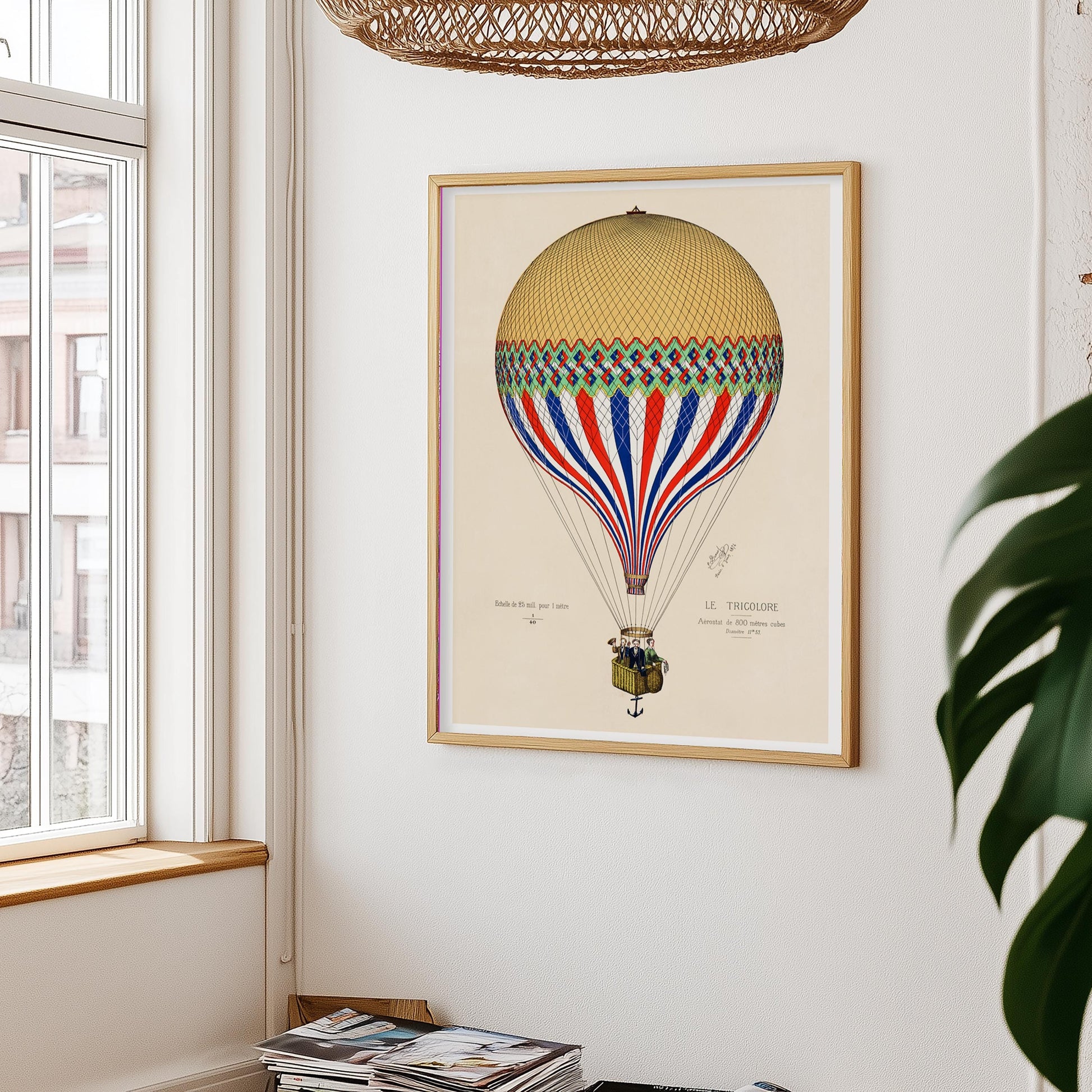 Luchtballonposter aan witte muur, met links een raam en rieten lampenkap erboven – plant rechts in beeld