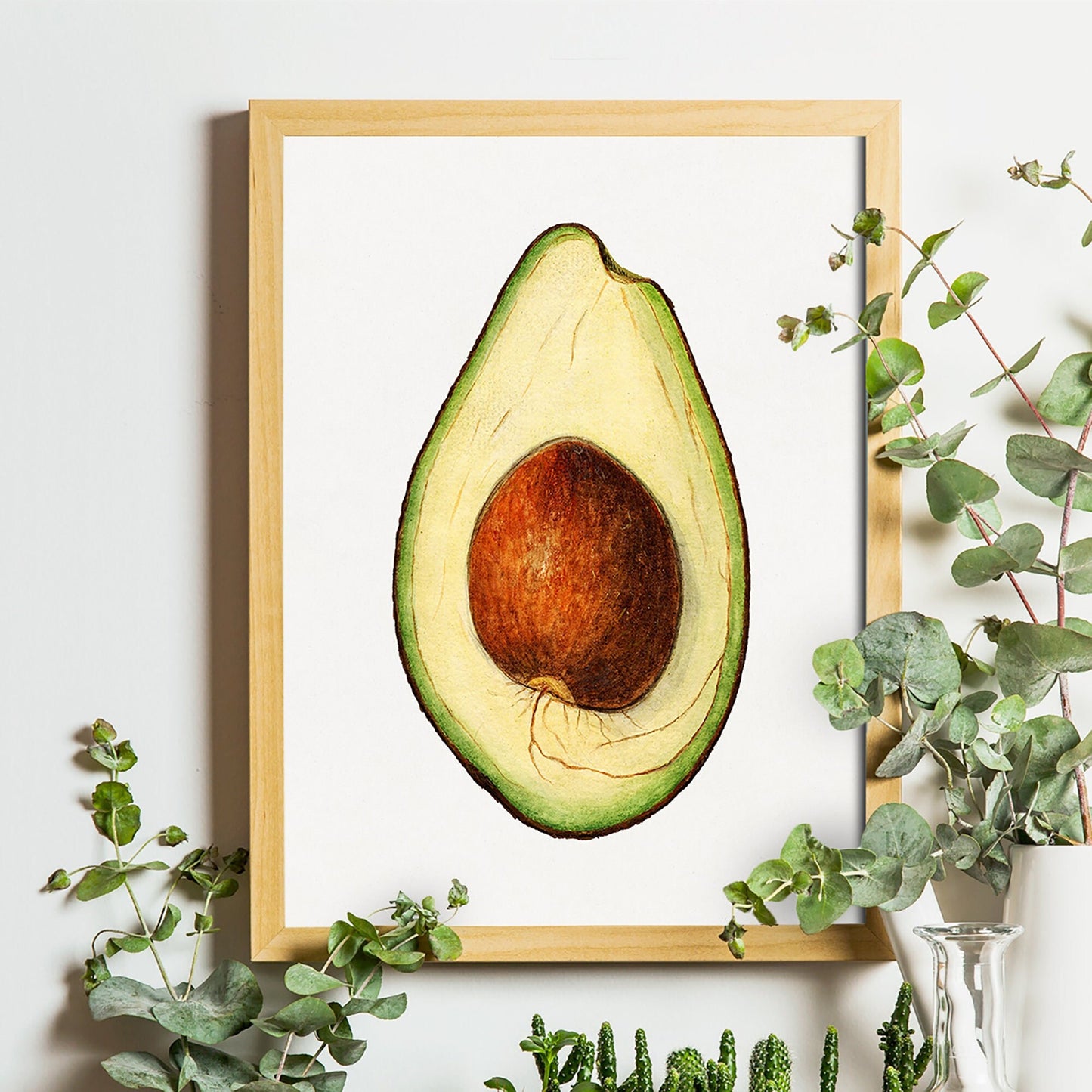 Ingelijste avocado poster aan een lichte muur, omringd door eucalyptus takjes in vaasjes.